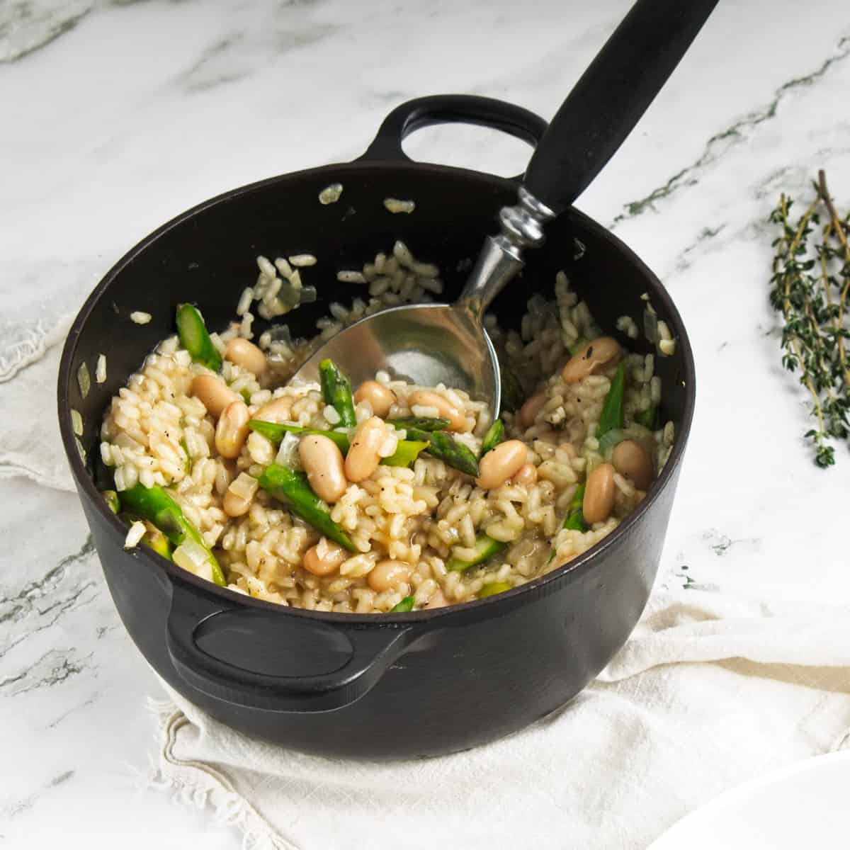 White bean risotto in black saucepan with serving spoon.