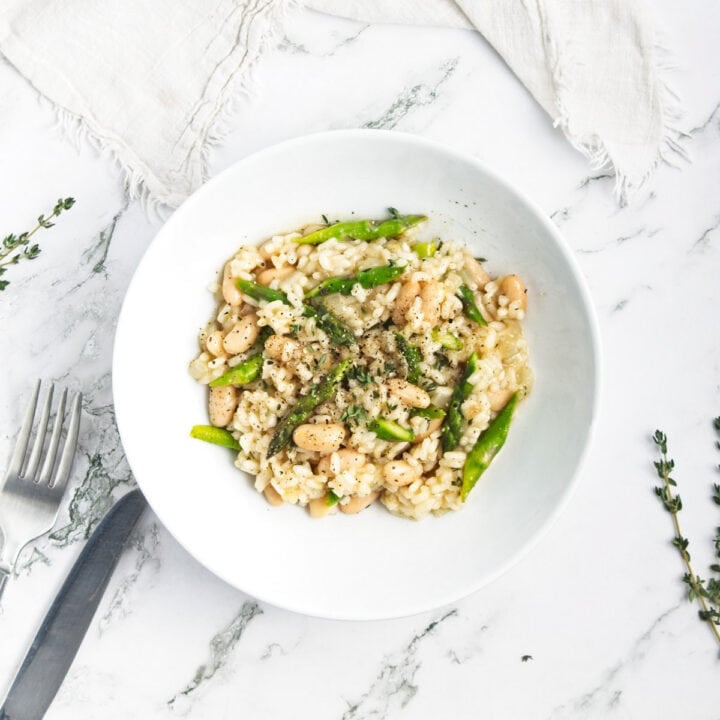 Shallow bowl of risotto topped with asparagus with sprigs of fresh thyme on the table.