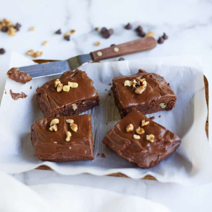Frosted chocolate brownies topped with walnut cooling on a parchment lined bakling sheet.