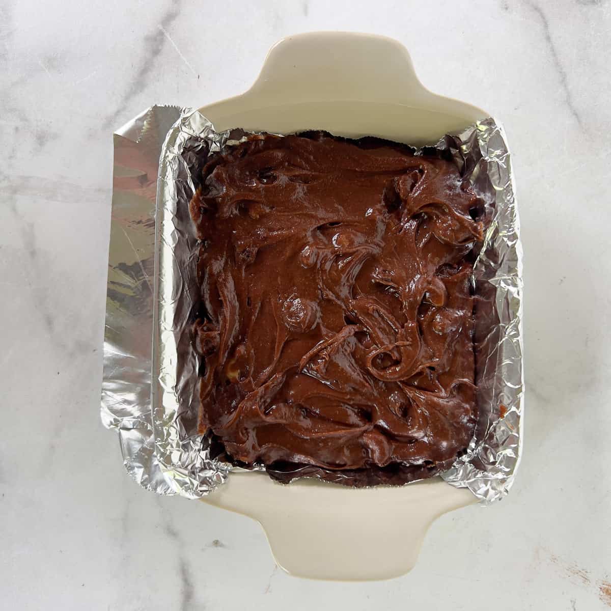 Brownie batter in small foil line baking dish.