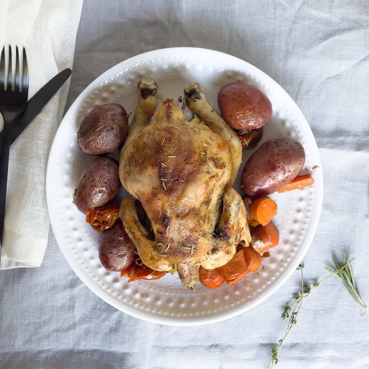 Roasted cornish hen on white plate with potatoes and carrots.