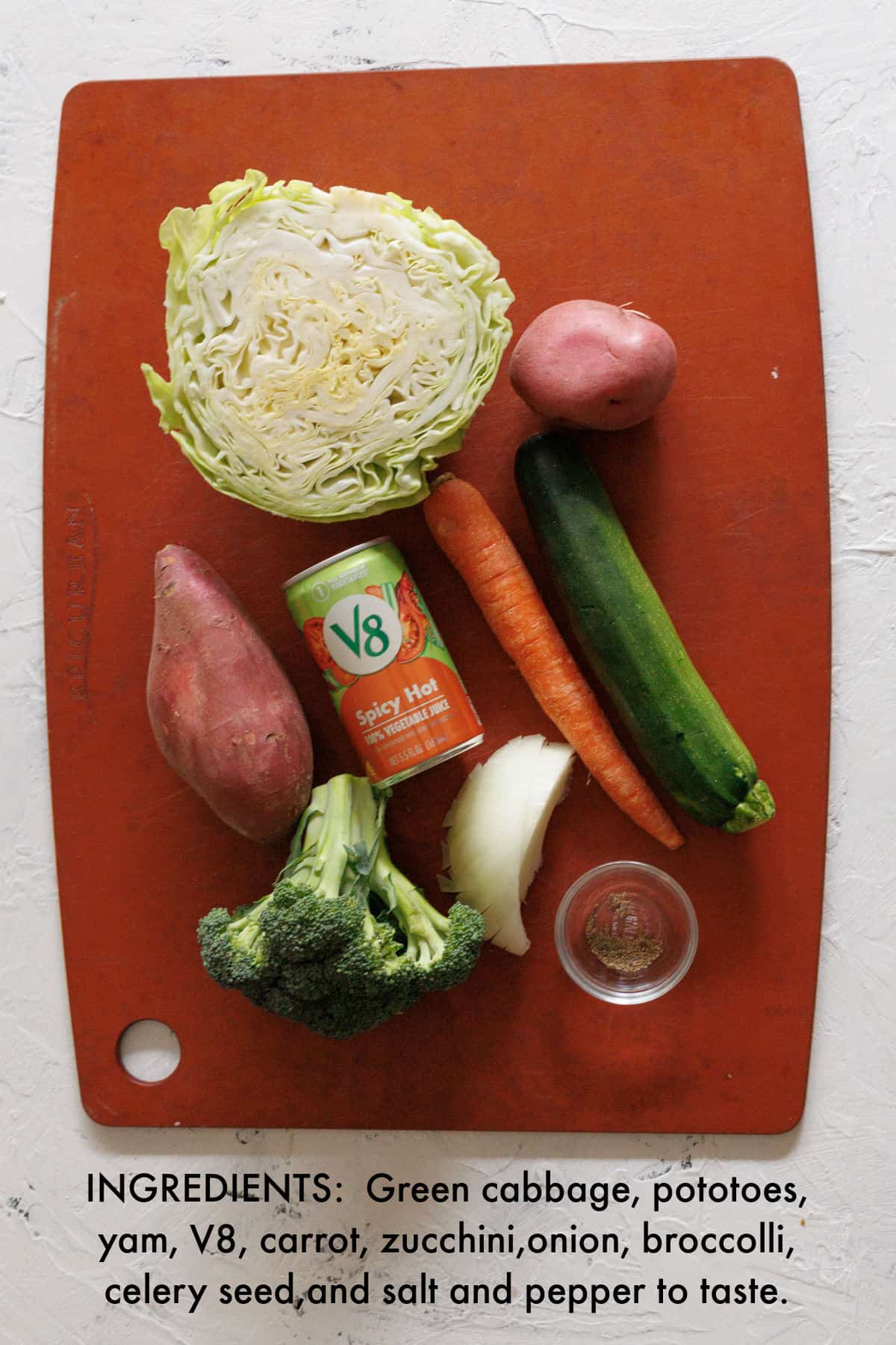Cabbage, potatoes, yam, V8 juice, carrot, zucchini, broccoli and celery seed on cutting board.