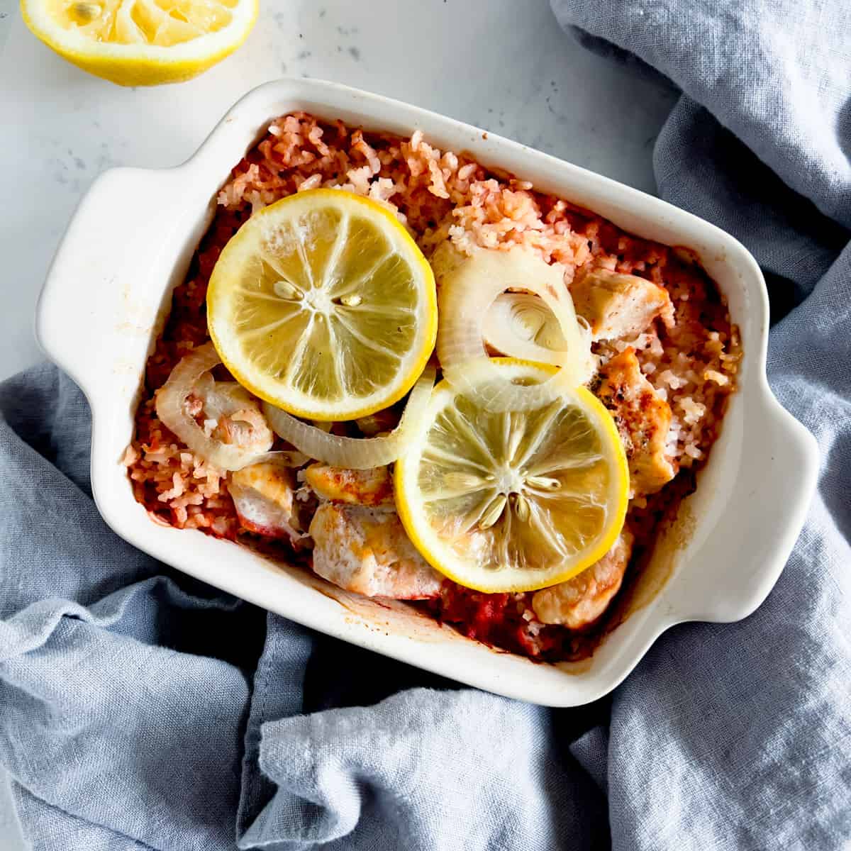 Lemon chicken casserole topped with lemon slices in a small white casserole dish.