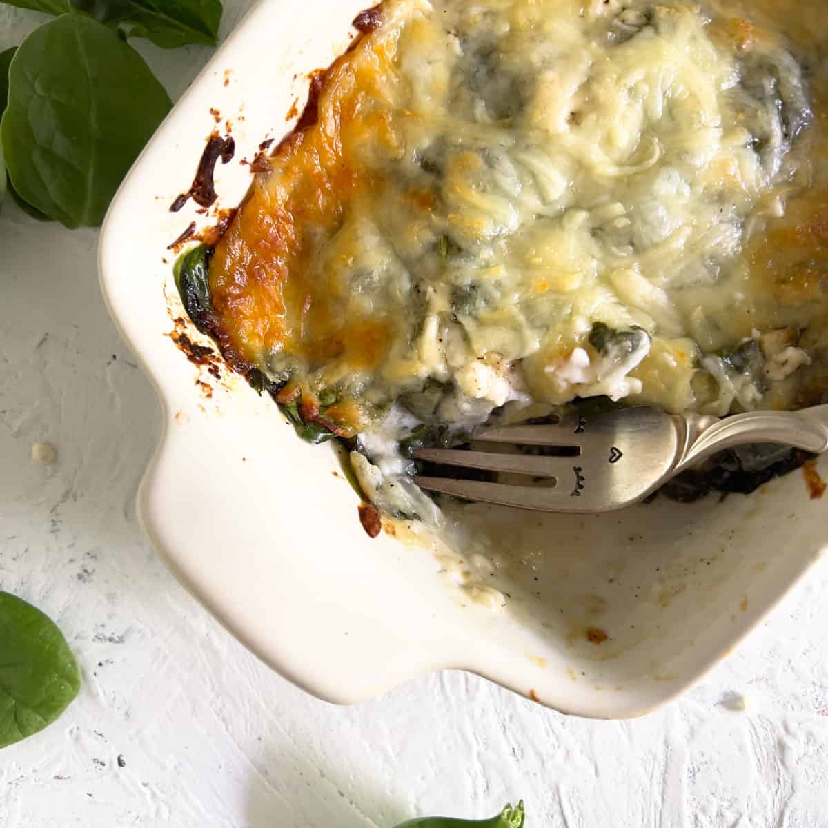 Mini spinach casserole in white baking dish with fork bite taken out.