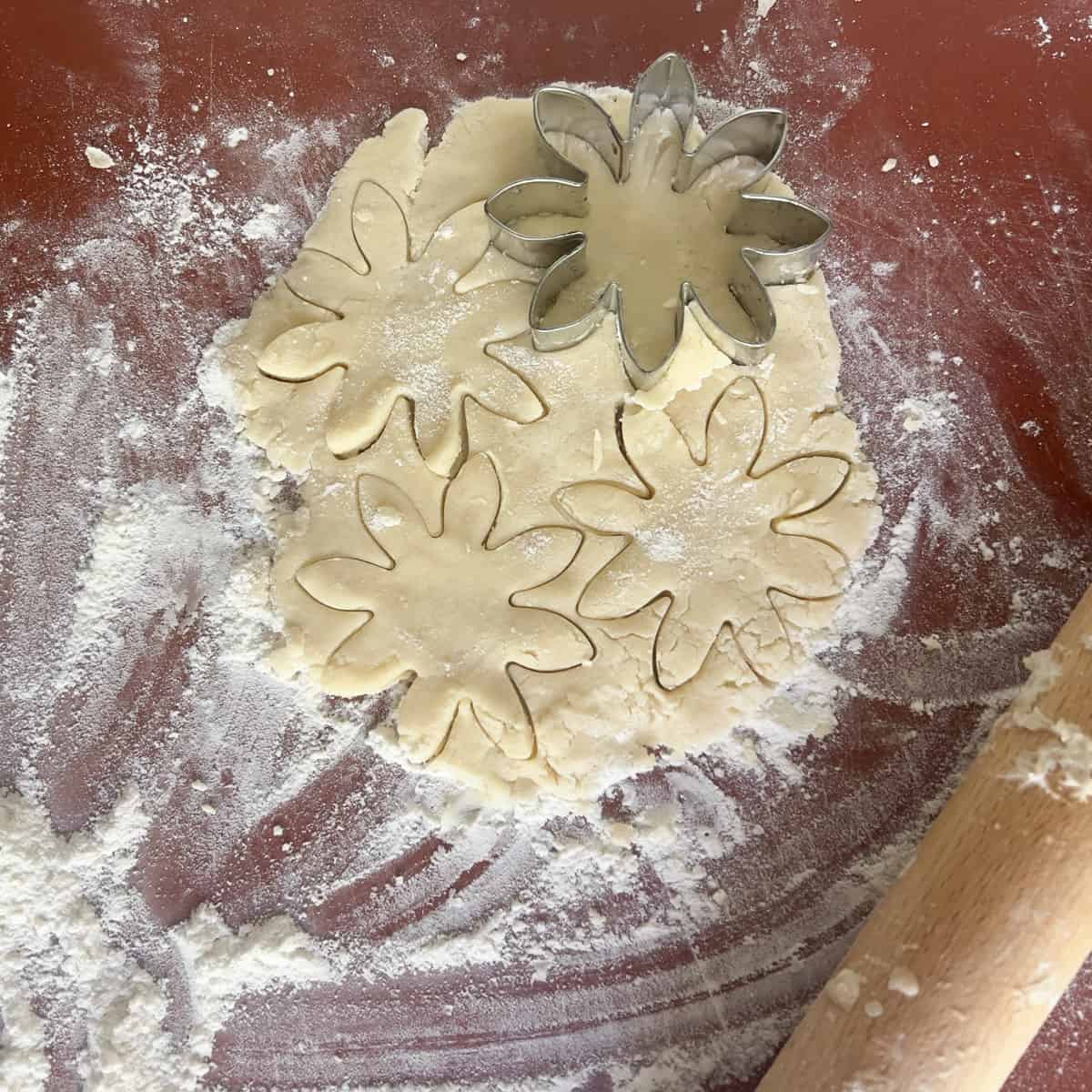 Butter cookie dough rolled out and cut out in daisy shape.