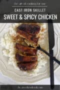 Sweet and Spicy chicken over bed of rice on white plate with black knife and fork on the side.