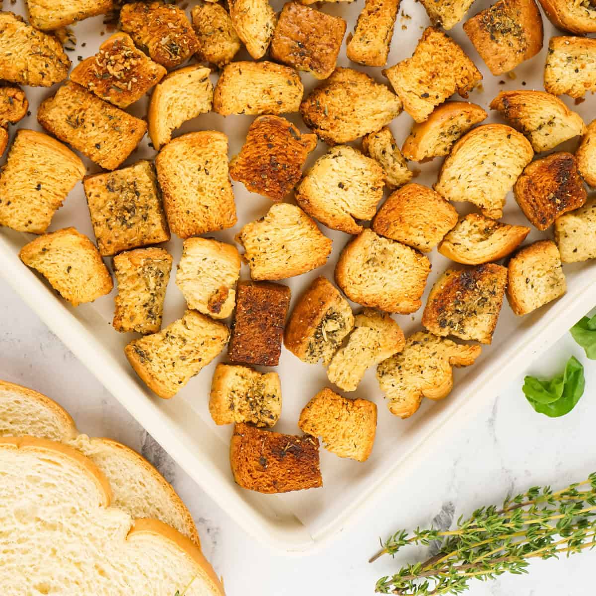 Baked homemade crouton on baking sheet with fresh bread on side.