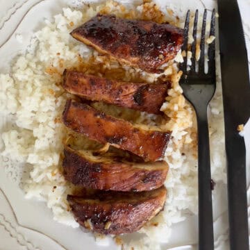 Pan seared chicken over rice on white plate.