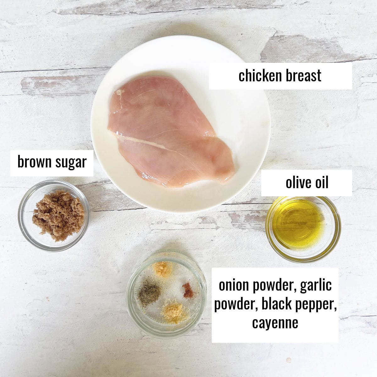 Uncooked chicken and spices measured out of white wood surface.