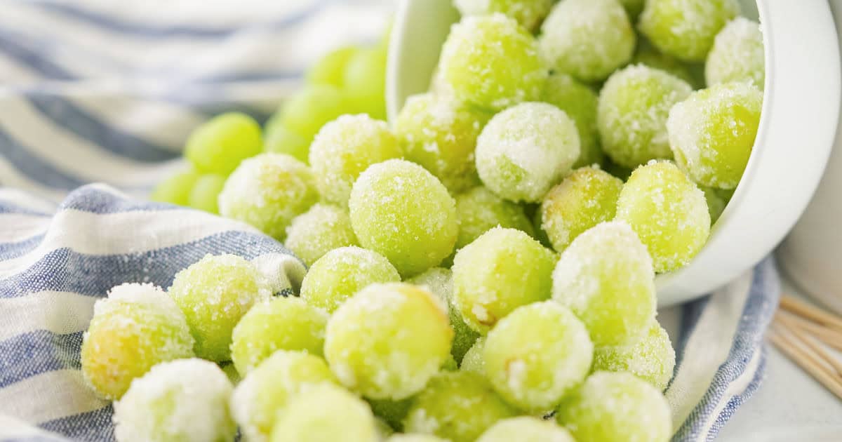 Sugar coated green grapes spilling out of a tipped bowl.