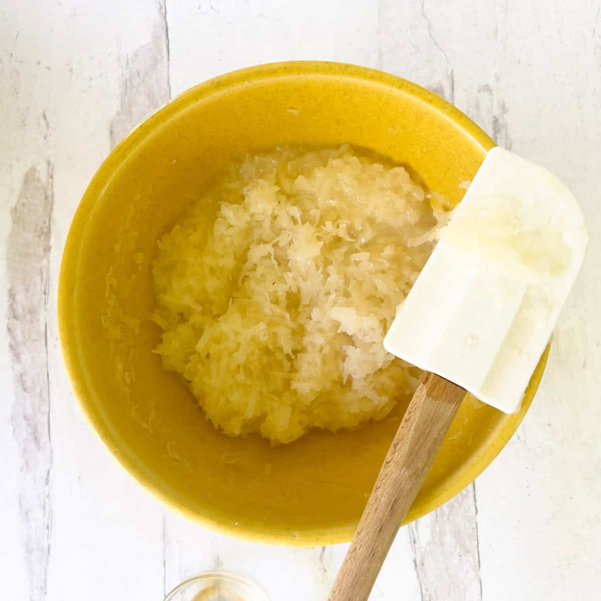 Coconut and egg white mixture in yellow bowl with rubber spatula on side.