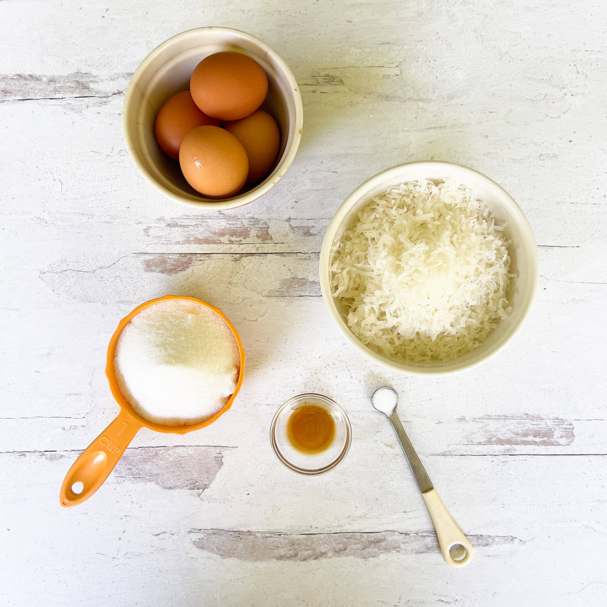 Bowl of eggs, shredded coconut, sugar, vanilla and salt.