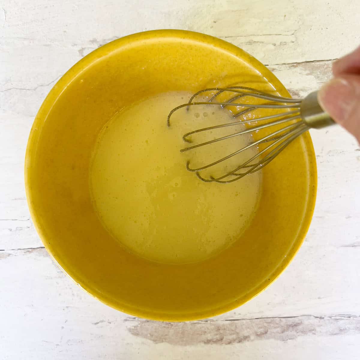 Sugar and egg whites whisked in a yellow bowl.