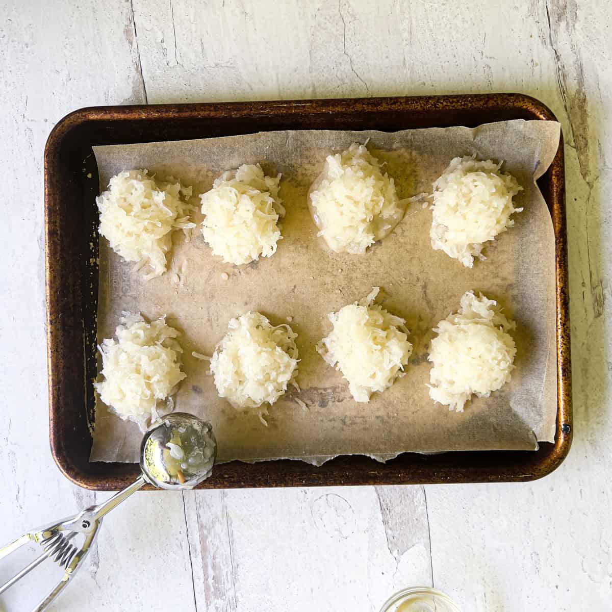 Unbaked coconut macaroons on parchment lined baking sheet.