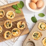 MIni spinach quiche on cooling rack woith muffin tin partially filled with baked mini quiche.