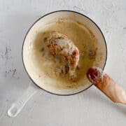 Chicken leg simmering in a mushroom sauce in a white skillet.