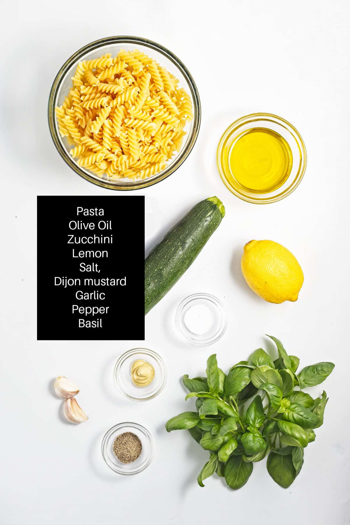 Pasta, lemon, fresh basil, olive oil, garlic and seasoning measured out on table.