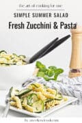 Zucchini and pasta salad on square plate with pepper grinder on table.