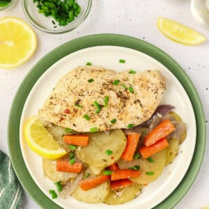 Plate of baked chicken and vegetable with green napkin and lemon slices on table.