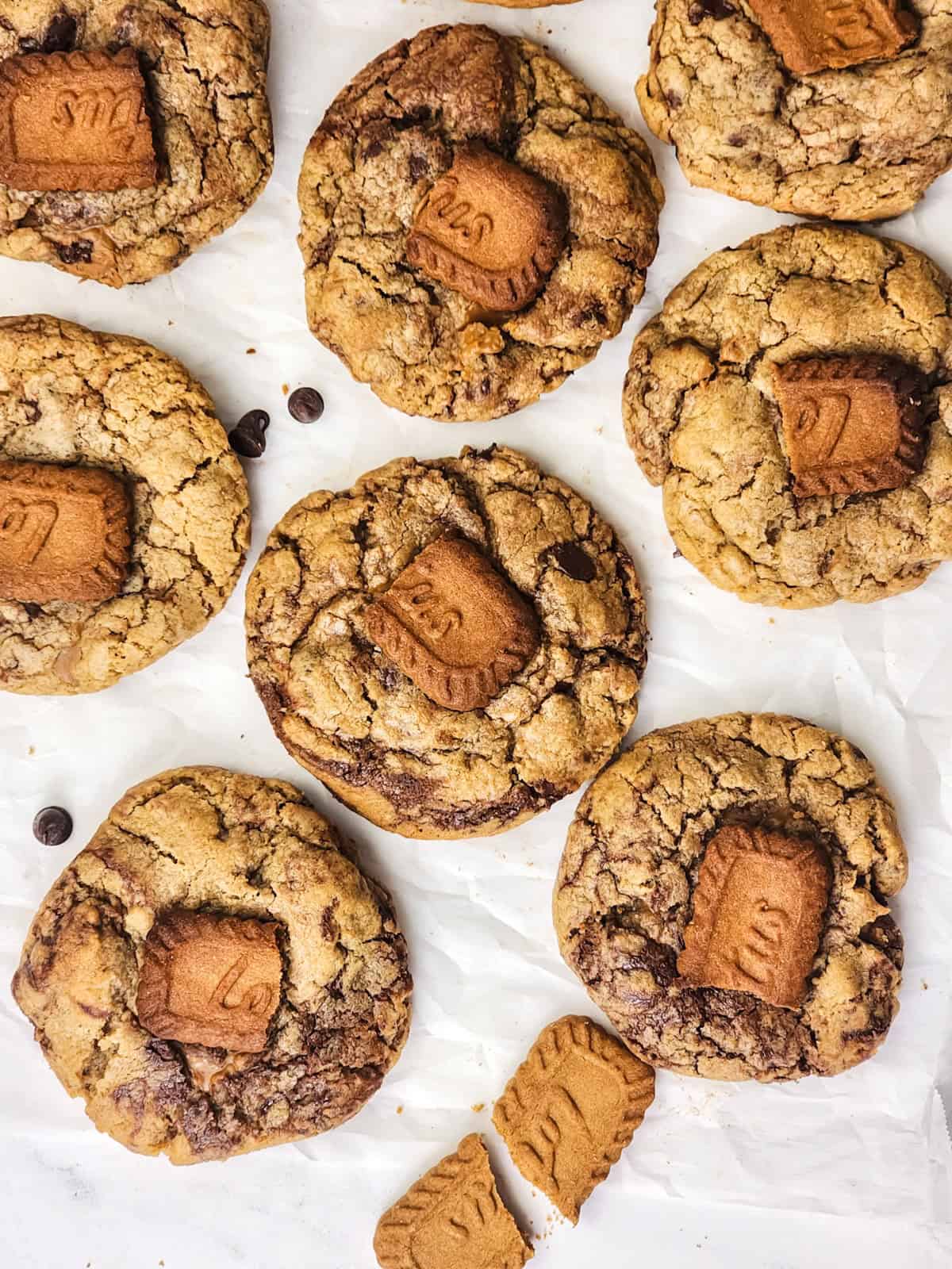 Biscoff chocolate chip cookies on parchment paper with crumbled Biscoff cookie on top.