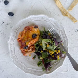 Chicken enchilada and green salad on white plate. Stips of tortilla and olives on table..