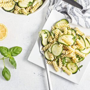 Fresh sliced zucchini and pasta salad on square plate.
