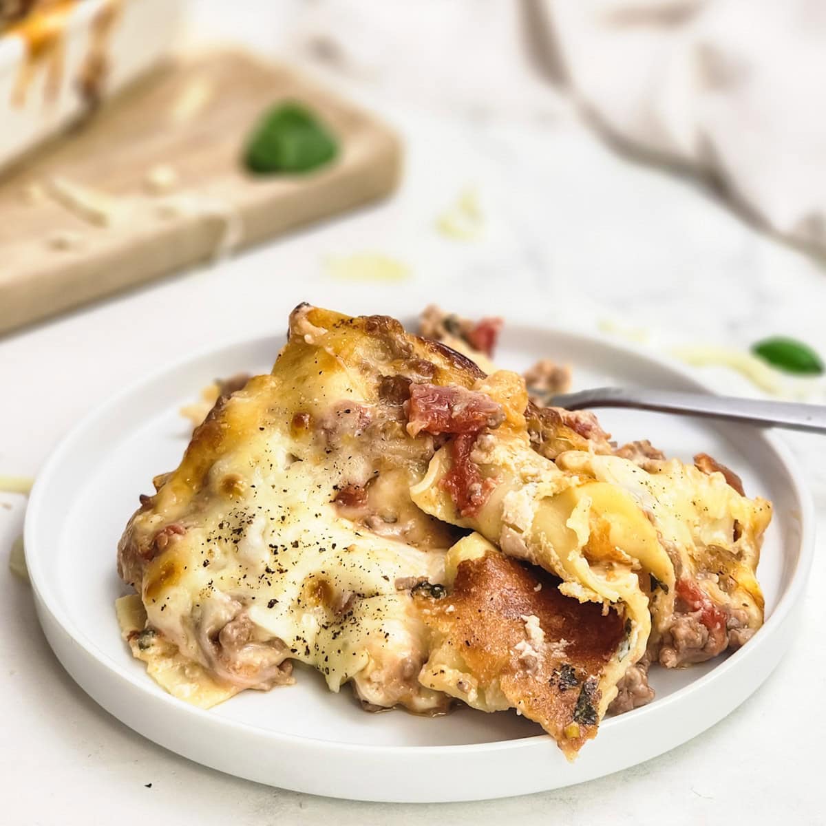 A serving of cheesy lasagna with meat sauce on a white plate, with a fork beside it.
