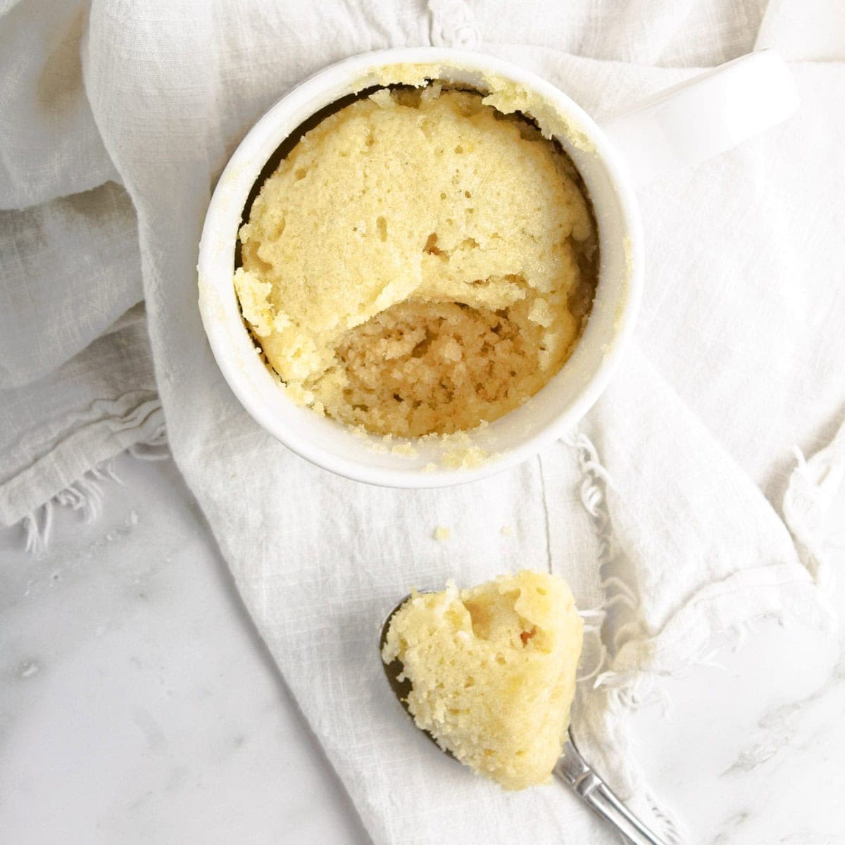 lemon cake in a mug with bite on spoon sitting on napkin.