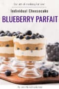 Two glass cups with layered blueberry parfaits, topped with fresh blueberries, on a wooden board.