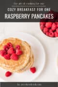 Stack of raspberry pancakes topped with fresh raspberries and syrup, with a fork cutting a piece; fresh raspberries beside.