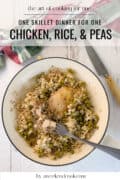 A skillet containing cooked chicken, rice, and peas with a fork, knife, and a towel nearby; text overlay describes it as a one-skillet dinner for one.