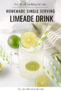 A mason jar filled with limeade, ice, lime slices, and a striped straw sits on a white surface, with whole and sliced limes and extra straws nearby.