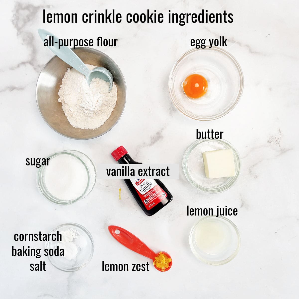 Top-down view of labeled lemon crinkle cookie ingredients: flour, egg yolk, butter, sugar, vanilla extract, lemon juice, cornstarch, baking soda, salt, and lemon zest.