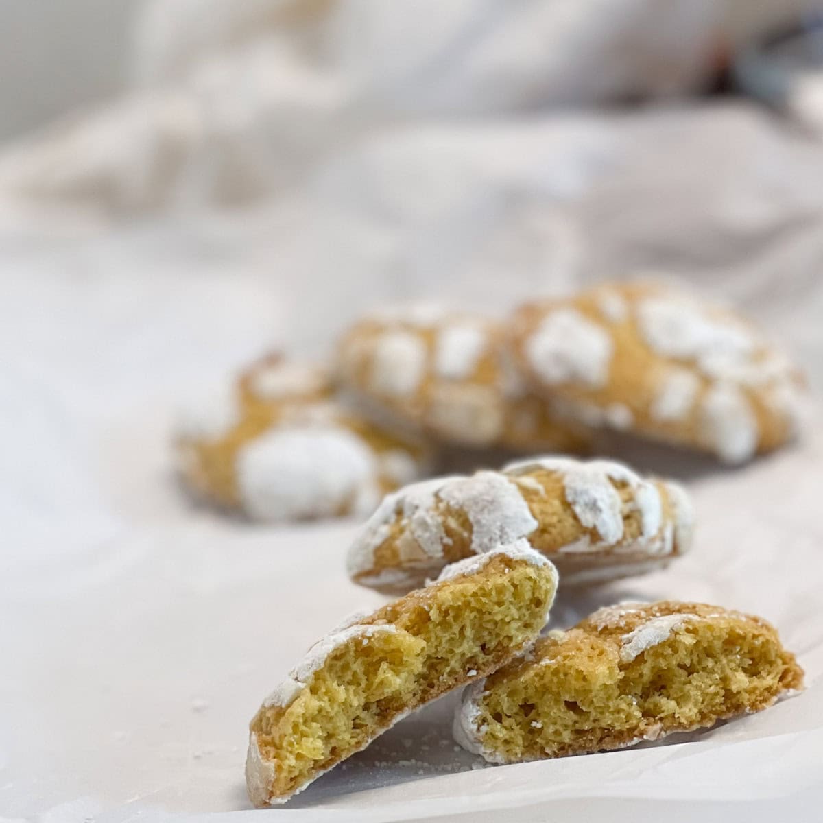 Several lemon crinkle cookies dusted with powdered sugar are arranged on parchment paper, with one cookie broken in half showing its soft interior.