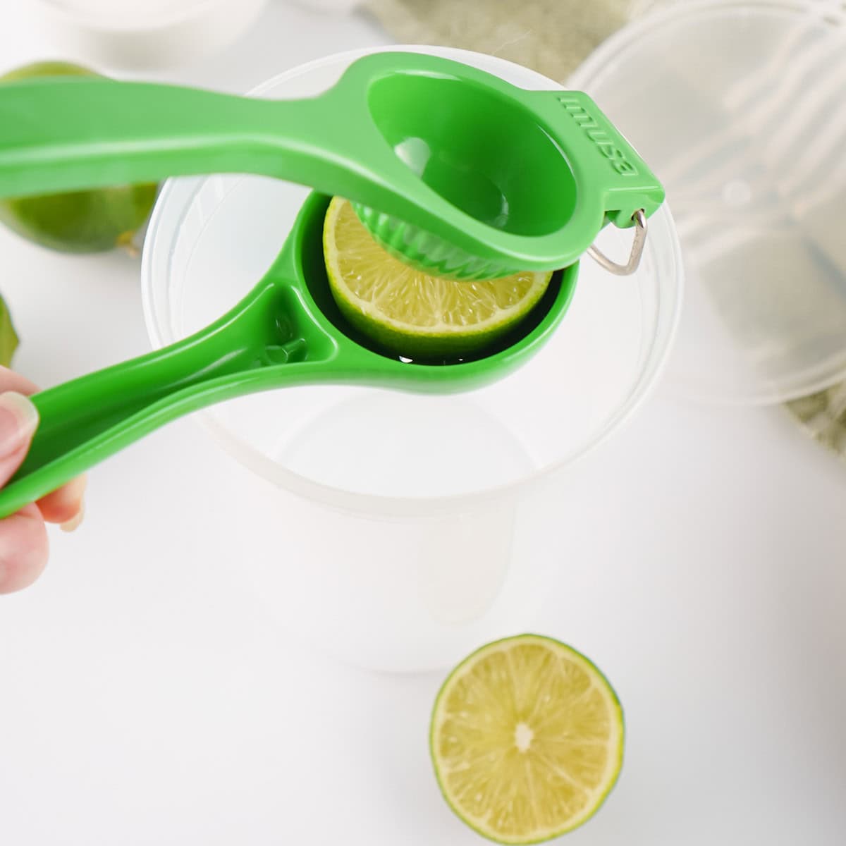 A person holding a green citrus squeezer over a bowl of limes.