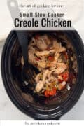 Shredded Creole chicken with vegetables in a small slow cooker, black spoon resting inside.
