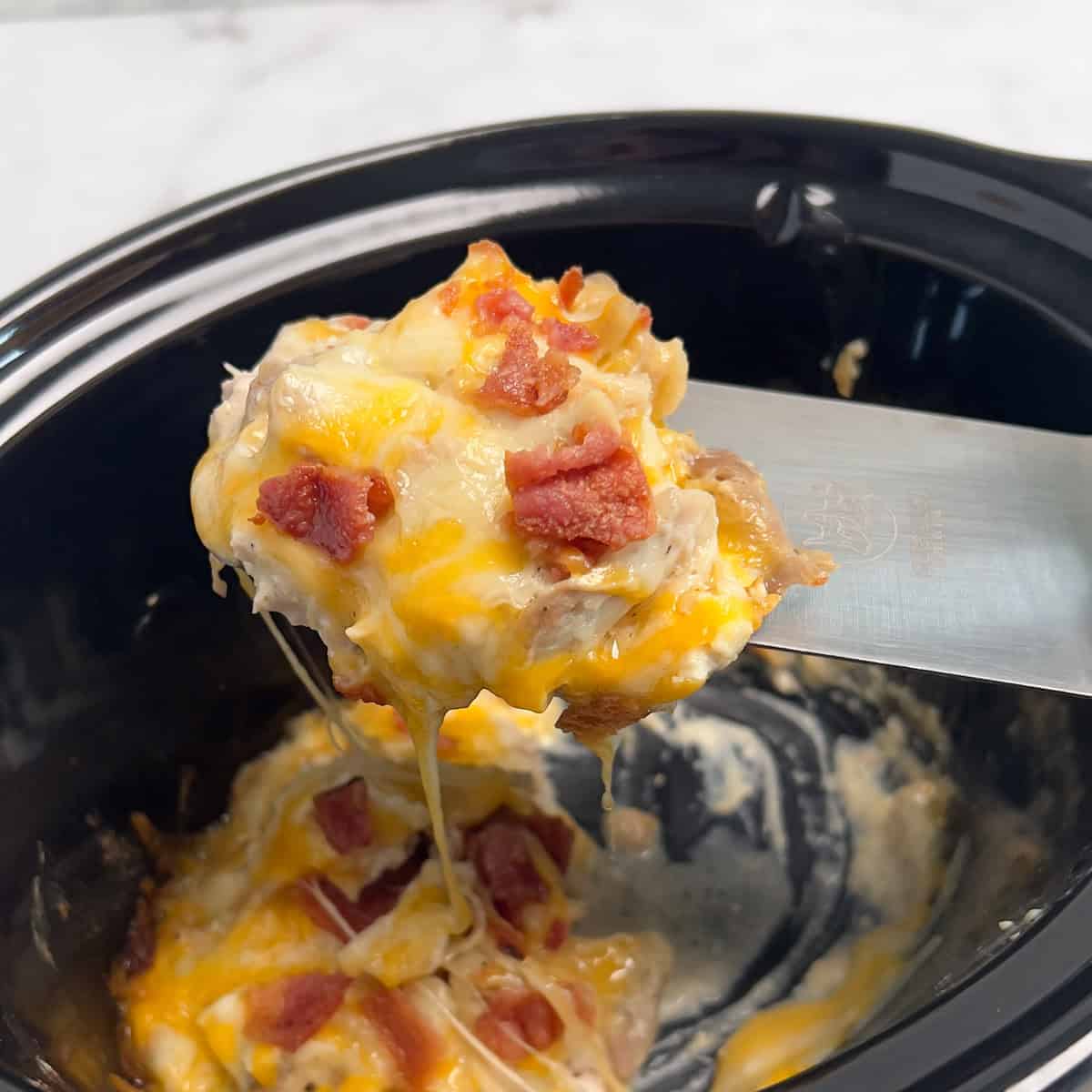 A crock pot with ranch chicken and portion lifted out on a spatula.