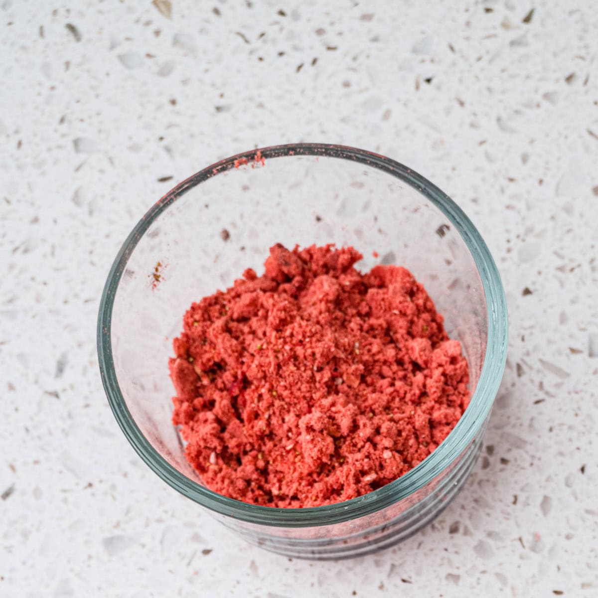 A clear glass bowl containing a mound of bright red, crumbly strawberry powder.