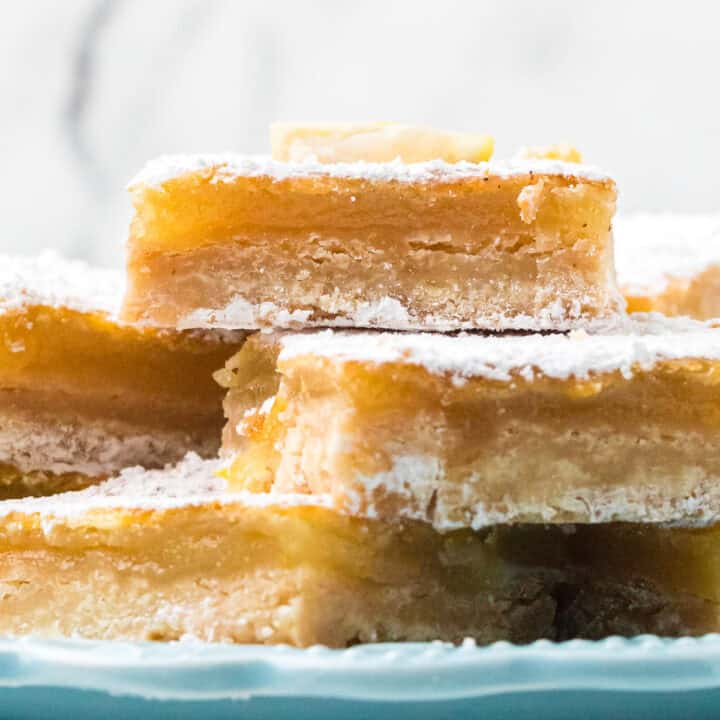A close-up of stacked lemon bars topped with powdered sugar on a blue plate.