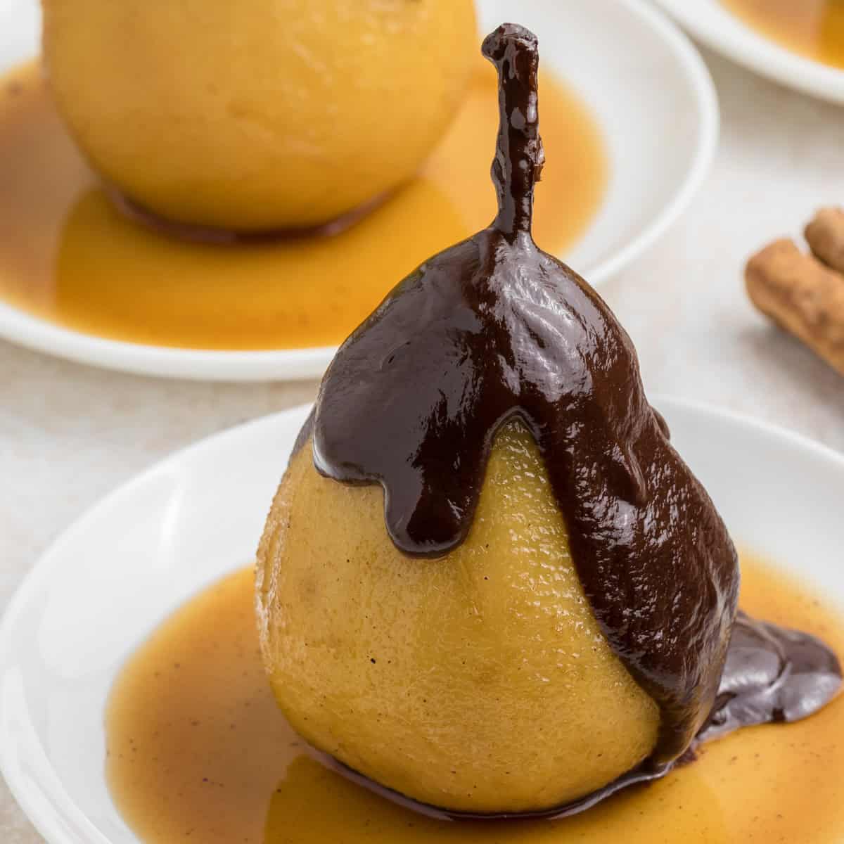 A poached pear on a white plate covered with chocolate sauce and surrounded by caramel sauce.