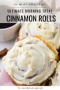 Close-up of frosted cinnamon rolls on a plate with a cup of sauce in the background. Text overlay reads, Ultimate Morning Treat Cinnamon Rolls.