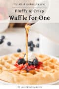 Syrup being poured onto a waffle topped with whipped cream, strawberries, and blueberries. Text overlay reads Fluffy & Crisp Waffle for One.