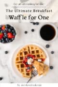 A plate with a waffle topped with berries and whipped cream, a fork, a bowl of strawberries and blueberries, and a cup of coffee on a white surface.