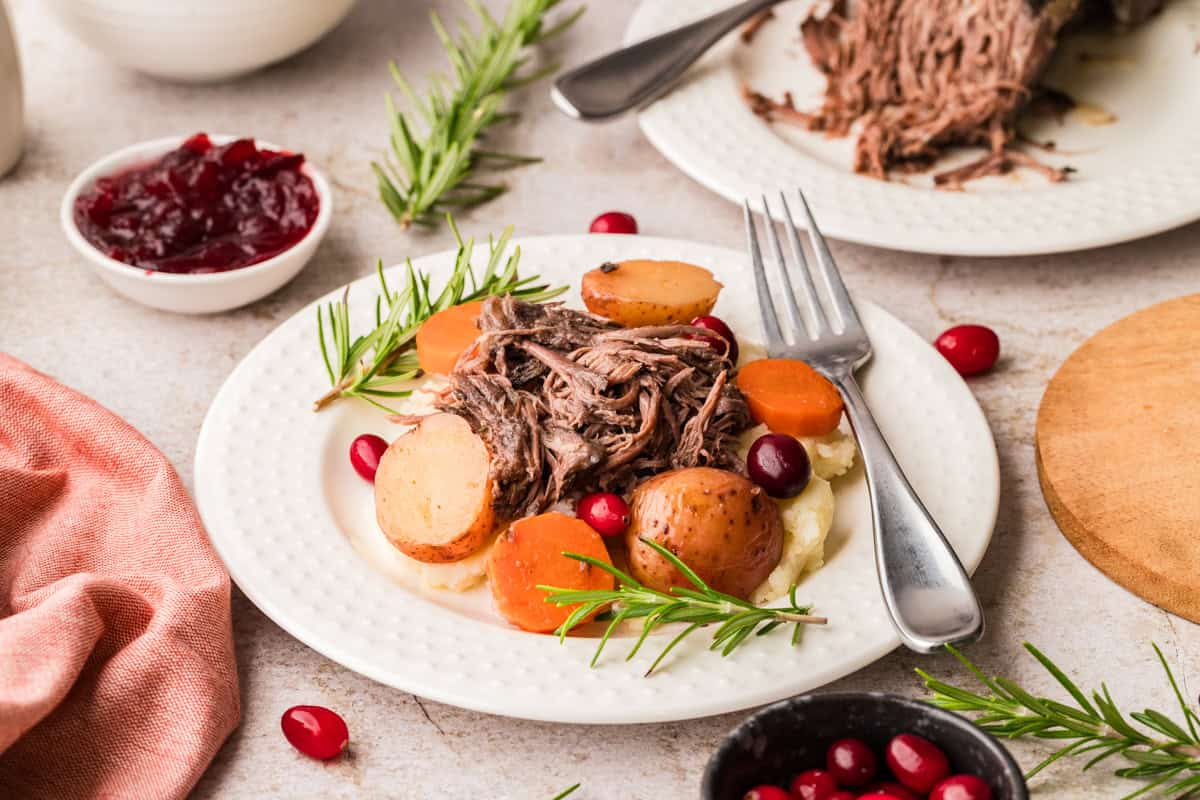 Shredded pot roast with cranberrries and sliced potatoes on white plate.