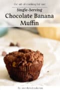 A single serving muffin, rich with chocolate and banana, sits on parchment paper as chocolate chips scatter in the background. Text reads: Single-Serving Chocolate Banana Muffin by aweekendcook.com.