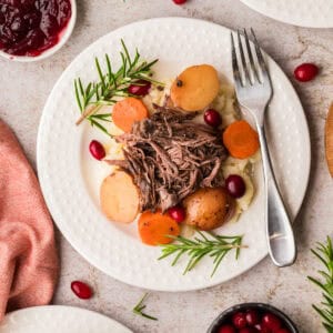 A plate with shredded beef, potatoes, carrots, and rosemary on mashed potatoes, surrounded by bowls of cranberries and cranberry sauce.