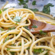 Cooked spaghetti mixed with chopped herbs and a light sauce, being stirred with a wooden spoon.
