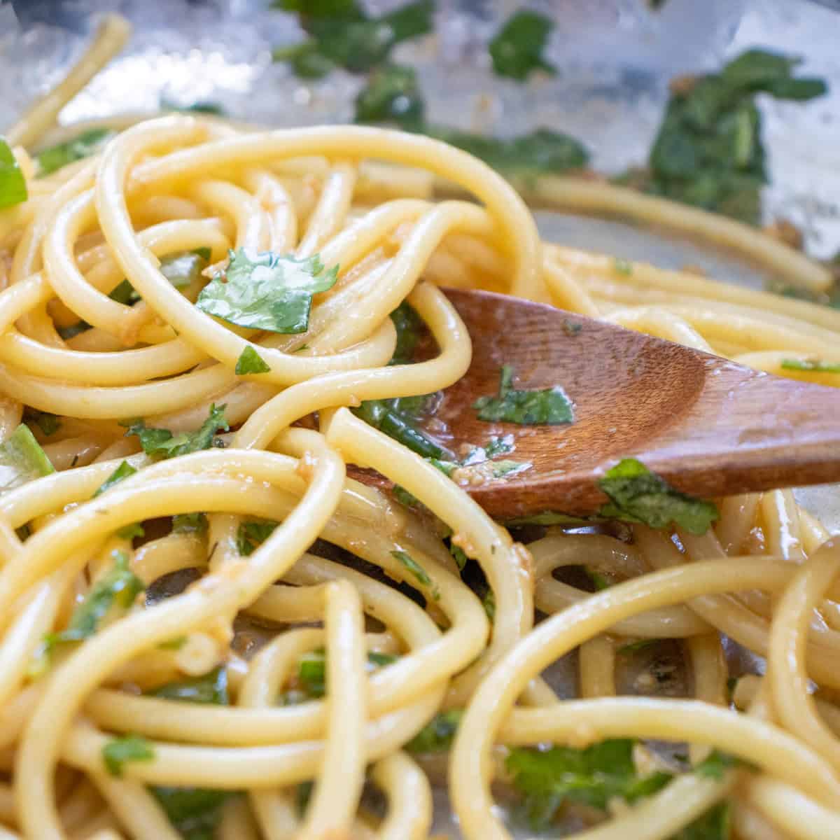 Cooked spaghetti mixed with chopped herbs and a light sauce, being stirred with a wooden spoon.