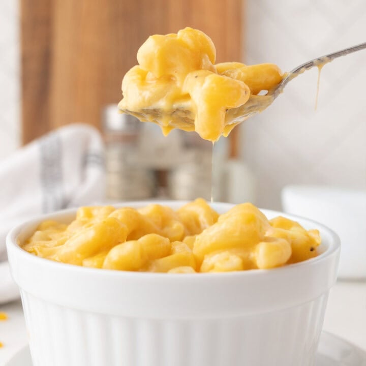 A spoon lifts creamy macaroni and cheese from a white ramekin, with melted cheese stretching between the spoon and the dish.