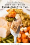 A fork holding a bite of turkey, green beans, sweet potato, stuffing, and a mini marshmallow, with a plate of Thanksgiving food in the background. Text overlay reads Thanksgiving for Two.